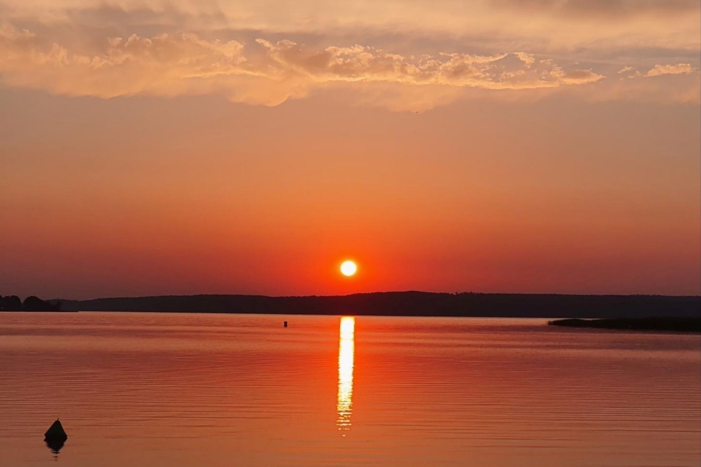 Ein Sonnenuntergang über ruhigem Gewässer mit einem kleinen Bojen im Vordergrund.