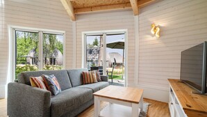 A modern living room with a grey sofa, a wooden coffee table, and a TV on a wooden cabinet. - Vacation home "Chiara" on Lake Tollensesee in the Mecklenburg Lake District (Penzlin)