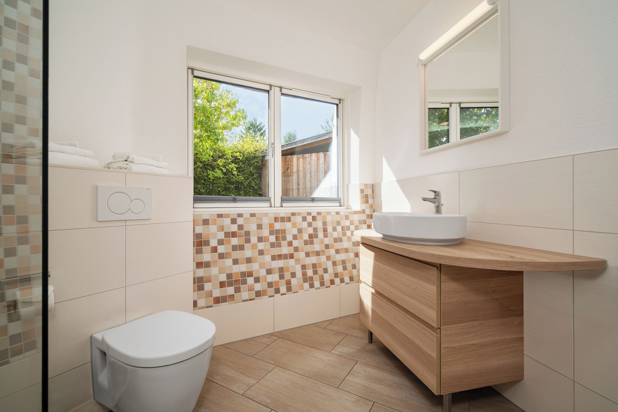 A modern bathroom with a white toilet, a wooden vanity with a sink, and a mosaic tile backsplash.
