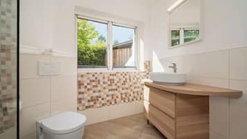 A modern bathroom with a white toilet, a wooden vanity with a sink, and a mosaic tile backsplash.