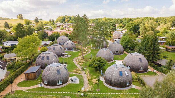 A cluster of dome-shaped buildings surrounded by lush greenery and a hilly landscape. - Vacation home "Chiara" on Lake Tollensesee in the Mecklenburg Lake District (Penzlin)