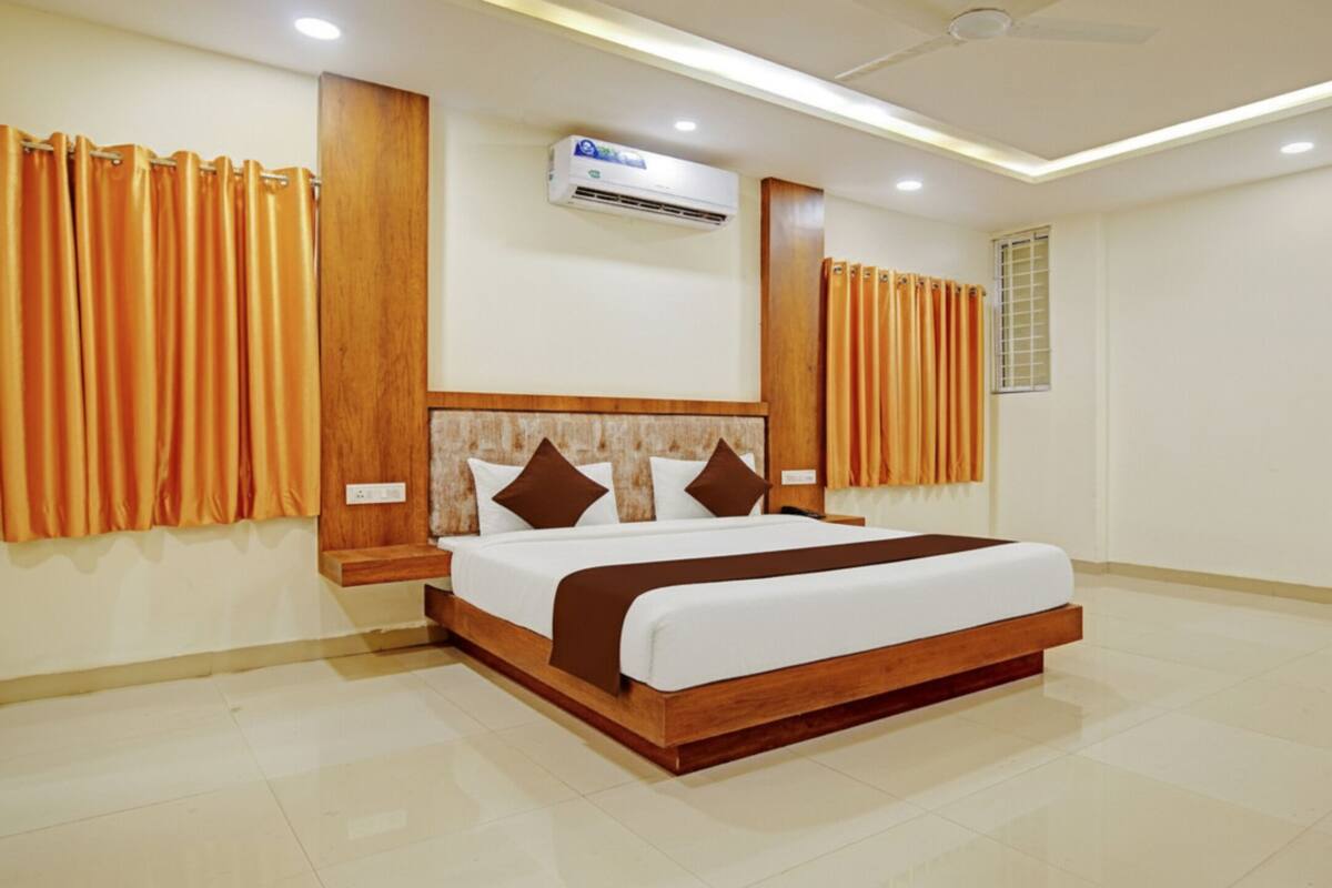 Une chambre d’hôtel moderne avec un grand lit, une tête de lit en bois et des rideaux orange.