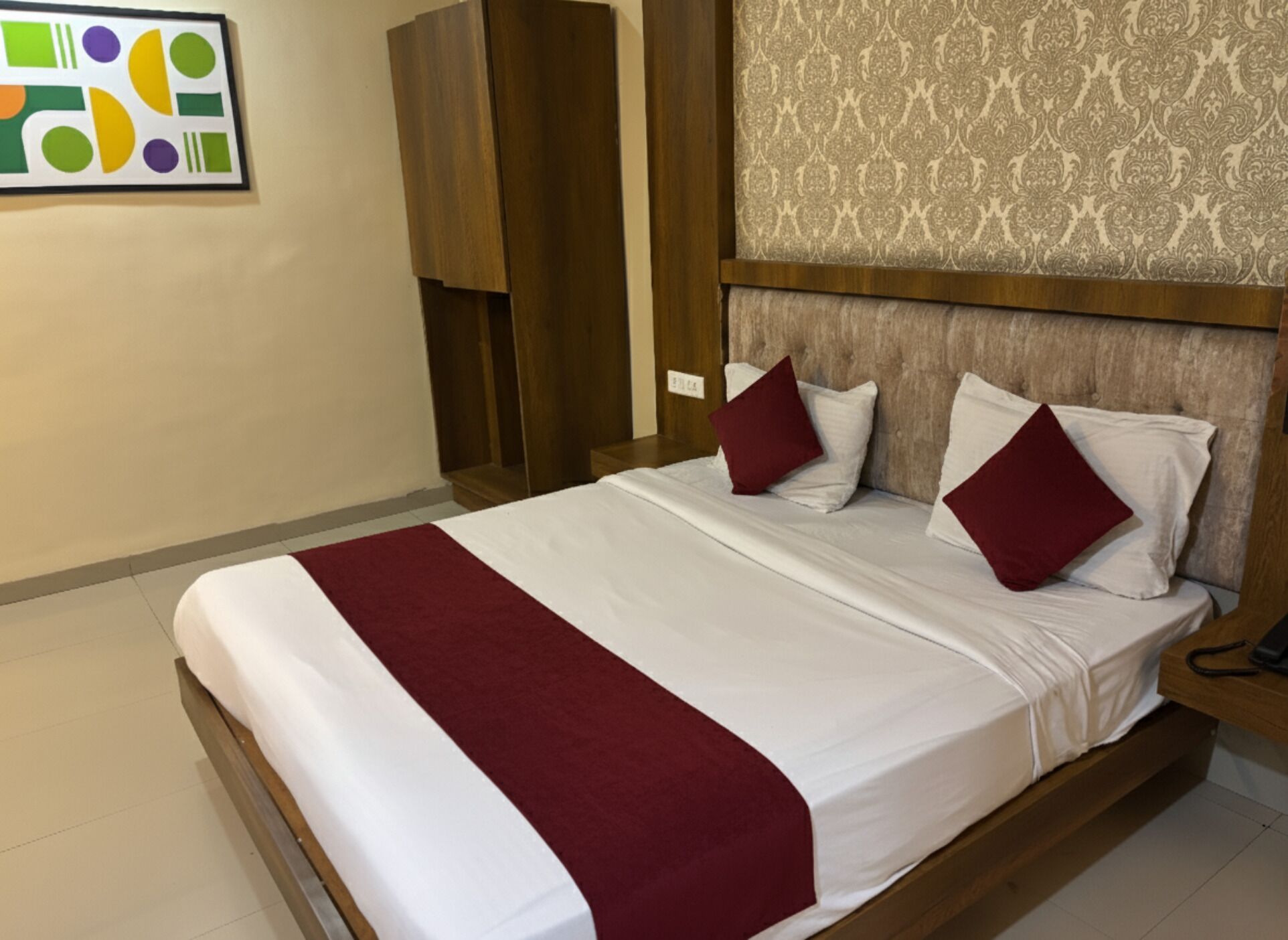 A hotel room with a large bed, a wooden headboard, a patterned wallpaper, and a modern abstract artwork on the wall.