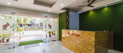 Zona de recepción con mostrador de mármol, ventilador de techo y plantas en macetas.
