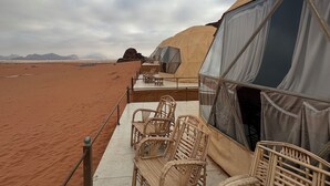 Tienda de campaña en el desierto con mobiliario de mimbre y vistas al paisaje desértico.