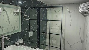 Une salle de bain moderne avec un pare-baignoire en marbre, un meuble-lavabo à deux vasques, des toilettes et une douche à parois de verre.
