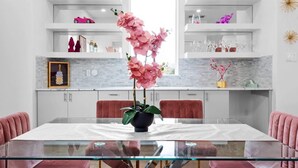 Una cocina moderna con una mesa de vidrio, sillas rosas y un florero con flores rosas.