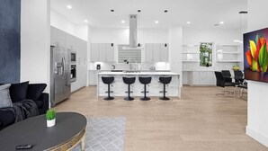 Una cocina moderna con una isla central, taburetes de bar y una zona de comedor con sillas.