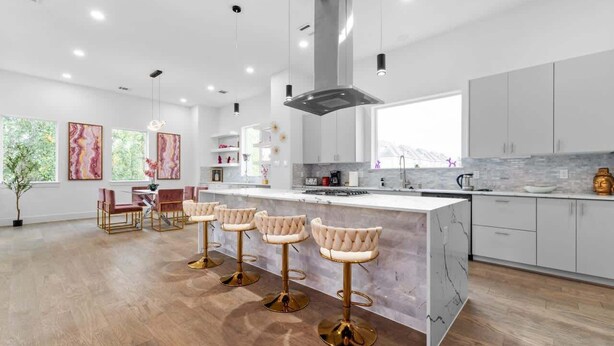 Una cocina moderna con una isla central, taburetes de bar y un comedor con sillas.