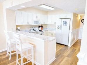 A kitchen with white cabinets, a marble countertop, a refrigerator, and a microwave. - Ashworth 405 (North Myrtle Beach)