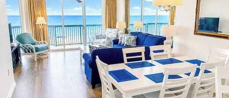Amplia sala de estar con balcón vista al mar, una mesa de comedor con sillas y un conjunto de sofás.