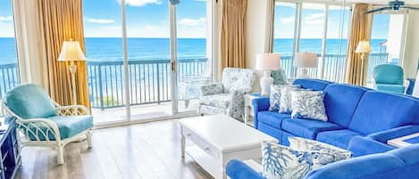 A spacious balcony with a view of the ocean, furnished with a blue sofa, a white armchair, and a white coffee table.
