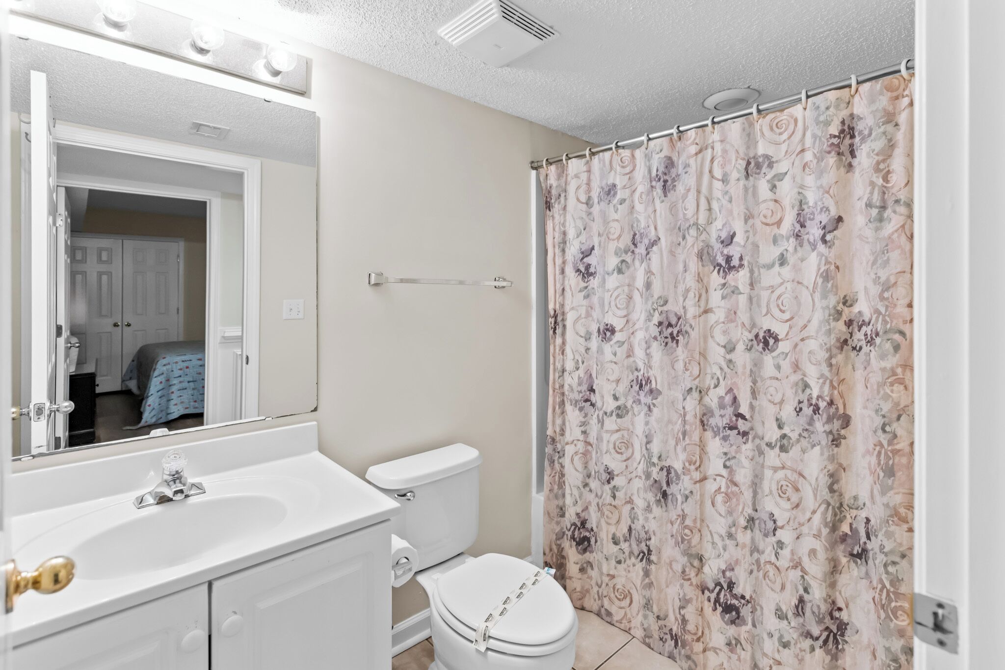 A bathroom with a white sink, toilet, and shower curtain with a floral pattern.