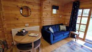 A wooden cabin interior with a round table, blue sofa, and a view through a glass door. - Snowdrop Lodge Dog Friendly Nr Anderby Creek (Alford)
