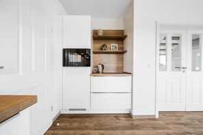 Een compacte keuken met witte kastjes, een houten aanrechtblad en een ingebouwde magnetron.