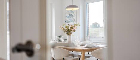 Un comedor con una mesa de madera, sillas blancas y una lámpara colgante.