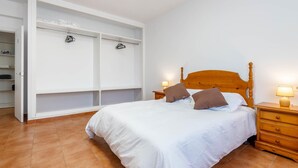 Une chambre à coucher avec un lit en bois, une literie blanche, une armoire avec espace pour suspendre les vêtements et une table de chevet avec une lampe.