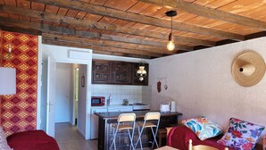 A cozy interior with a wooden ceiling, a kitchen area with a microwave and stove, a dining table with chairs, and a patterned wall.