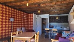 A cozy room with a wooden dining table, chairs, a sofa, and a kitchen area with cabinets and a microwave.