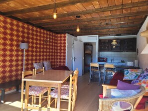 Quarto acolhedor com uma mesa de jantar de madeira, cadeiras, um sofá e uma área de cozinha com armários e micro-ondas.
