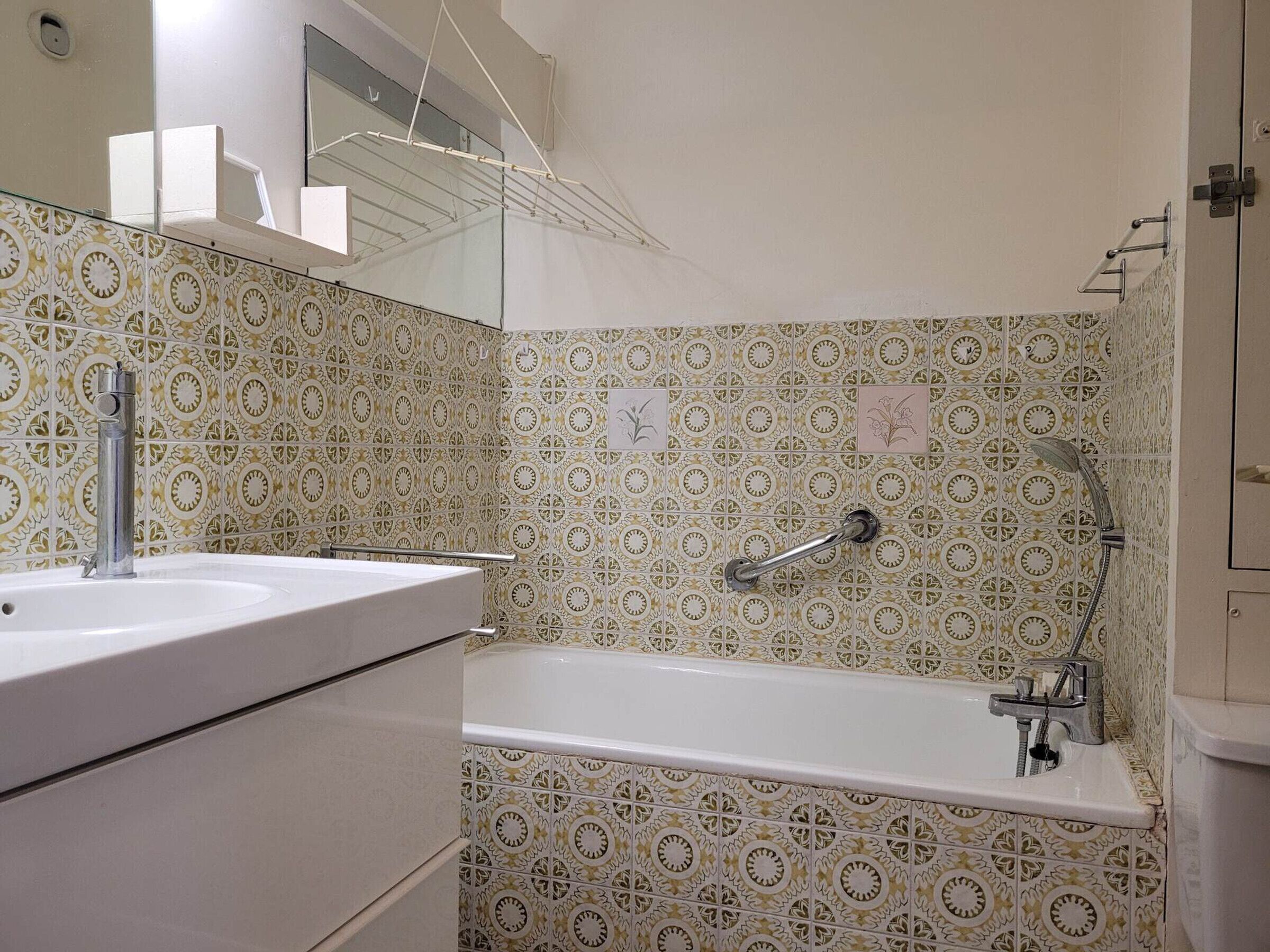 Een badkamer met patroontegels, een wastafel, een spiegel, een handdoekhouder en een douche.