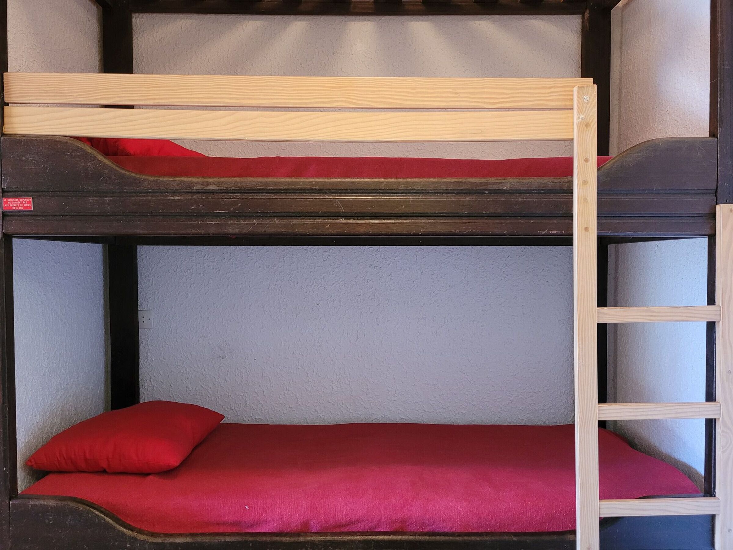 A bunk bed with two levels, each with a wooden frame and red bedding.