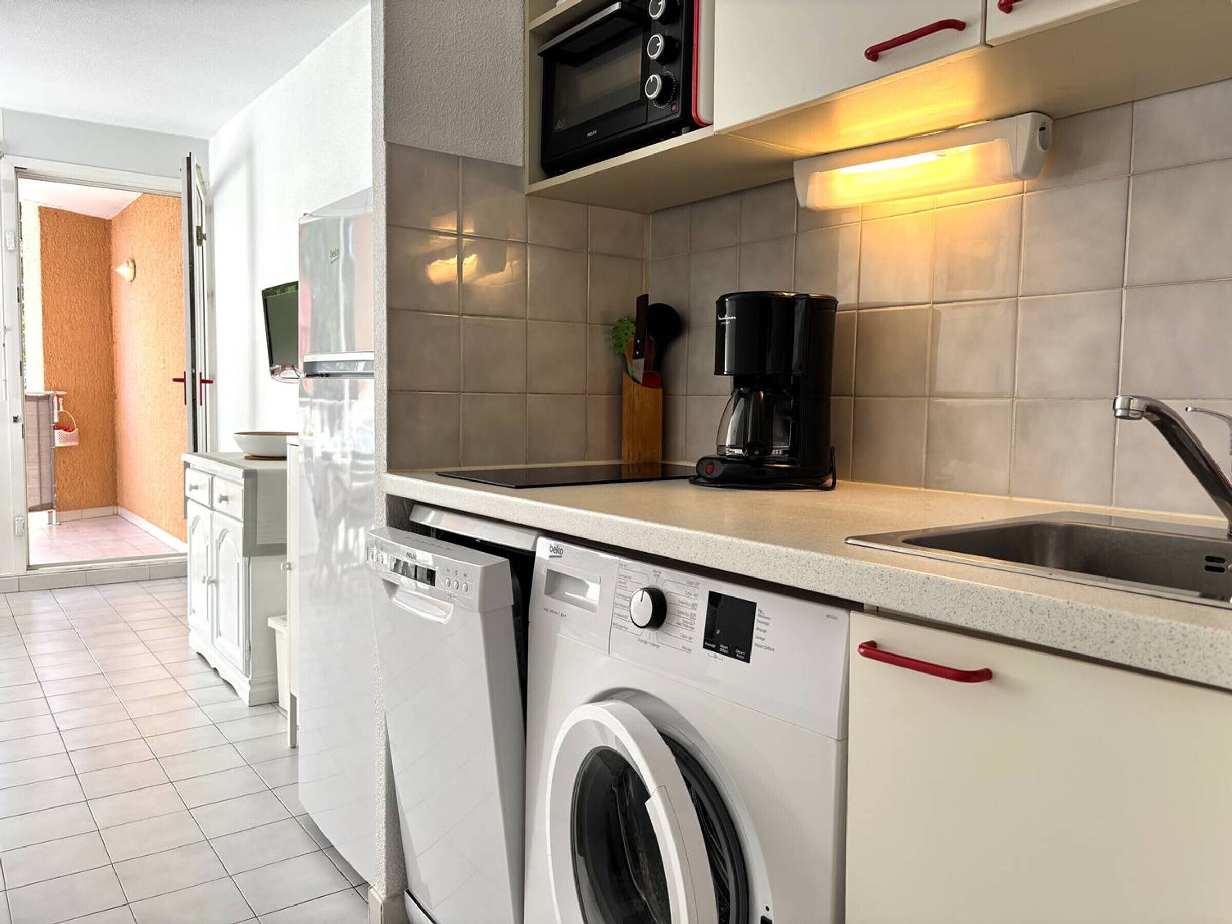 A compact kitchen with a washing machine, a coffee maker, and a microwave.