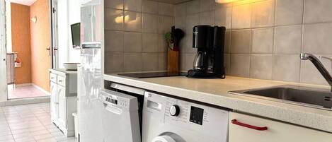 A compact kitchen with a washing machine, a coffee maker, and a microwave.