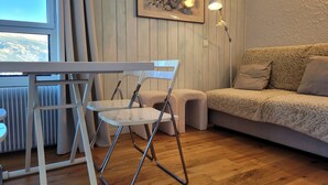 A modern living room with a white dining table, two white chairs, a beige sofa, and a framed floral artwork on the wall. - Renovated studio for 4, valley view, near slopes (Pra-Loup)