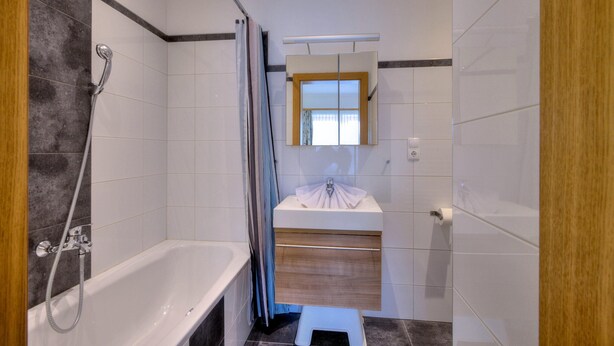 Une salle de bain moderne équipée d’une baignoire, d’une douche, d’un meuble-lavabo avec miroir et de toilettes.