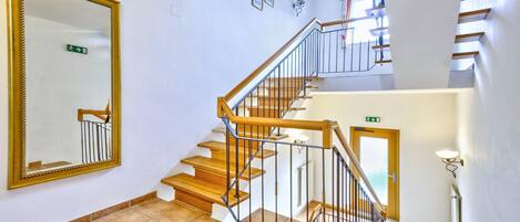 A staircase with wooden steps and metal railings, a large mirror on the wall, and a door with an exit sign.