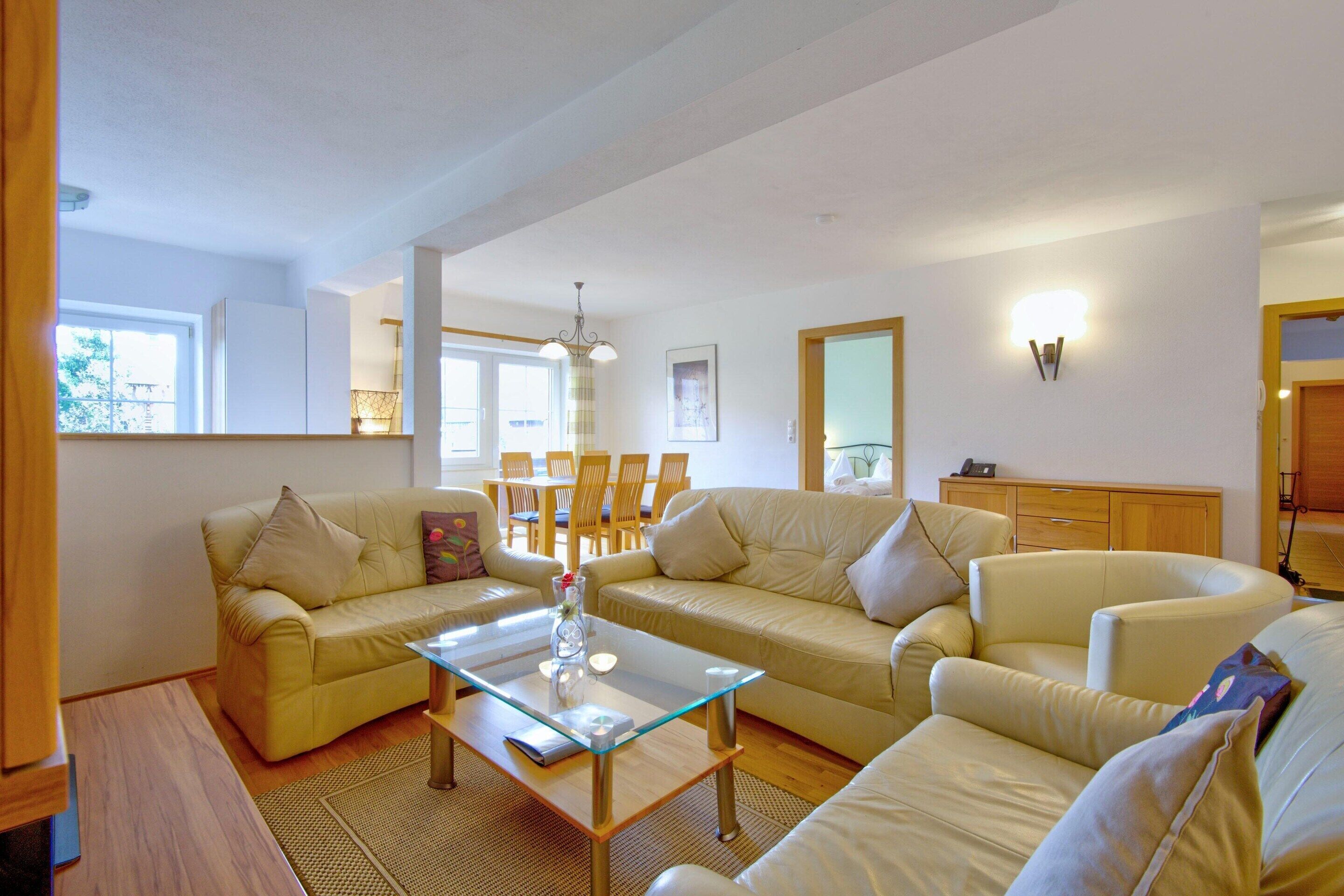 A living room with two sofas, a glass coffee table, and a dining area with chairs and a table.