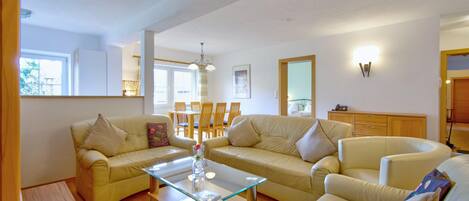 A living room with two sofas, a glass coffee table, and a dining area with chairs and a table.