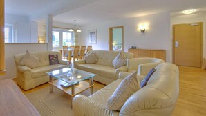 A spacious living room with a beige sofa set, a glass coffee table, and a wooden floor. There is a dining area with chairs and a table in the background. - Wildschonau Alpine Vicky Apartment (Wildschönau)