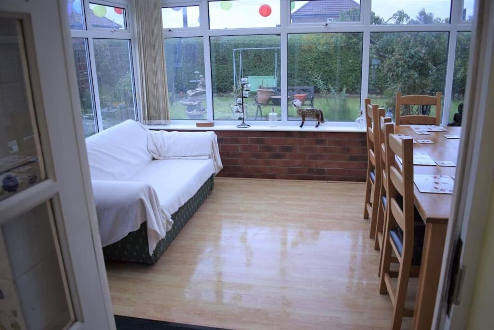 A room with a bed, a dining table with chairs, and a view of a garden through large windows.