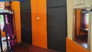 A room with two doors, one black and one orange, with a small window and a metal rack with clothes. - Rising Surya Homestay (Kushalnagar)
