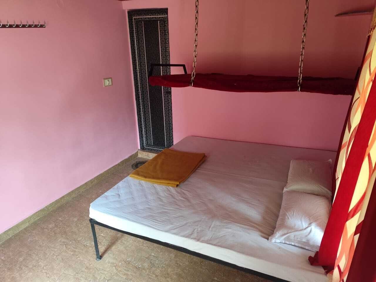 A single bed with a white mattress and a brown blanket, a small table with a yellow cloth, and a door with a metal handle.