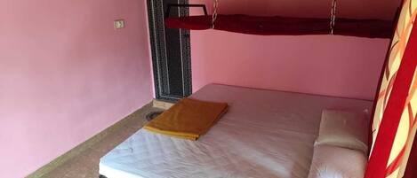 A single bed with a white mattress and a brown blanket, a small table with a yellow cloth, and a door with a metal handle.