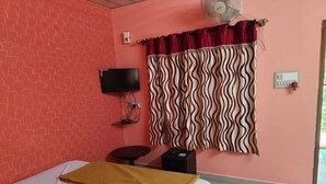 A room with a bed, a television, a power outlet, a fan, and a window with curtains. - Rising Surya Homestay (Kushalnagar)