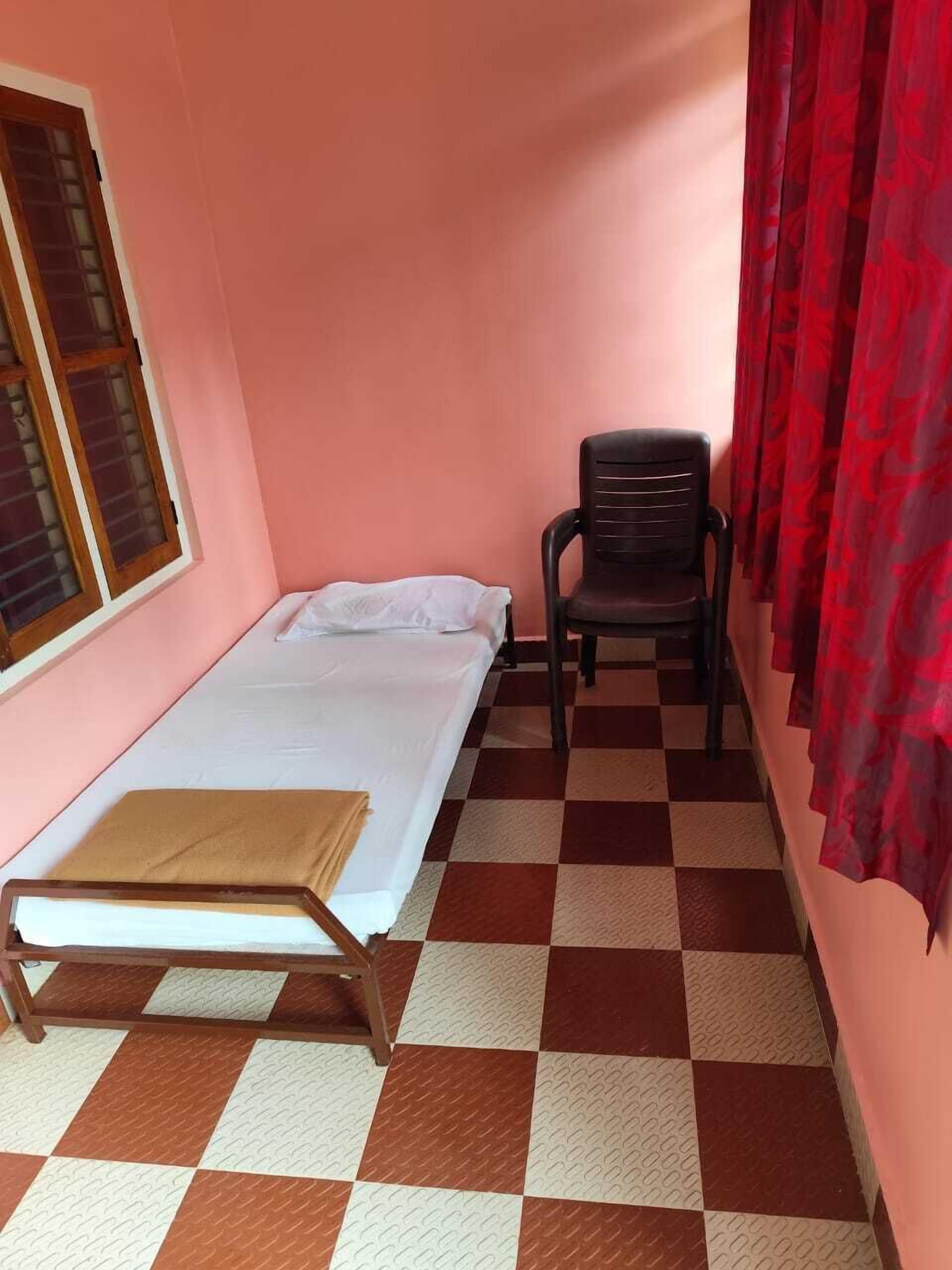 A small room with a single bed, a chair, and a window.