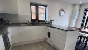 Una cocina moderna con lavadora incorporada, una ventana con persianas y un reloj en la pared.