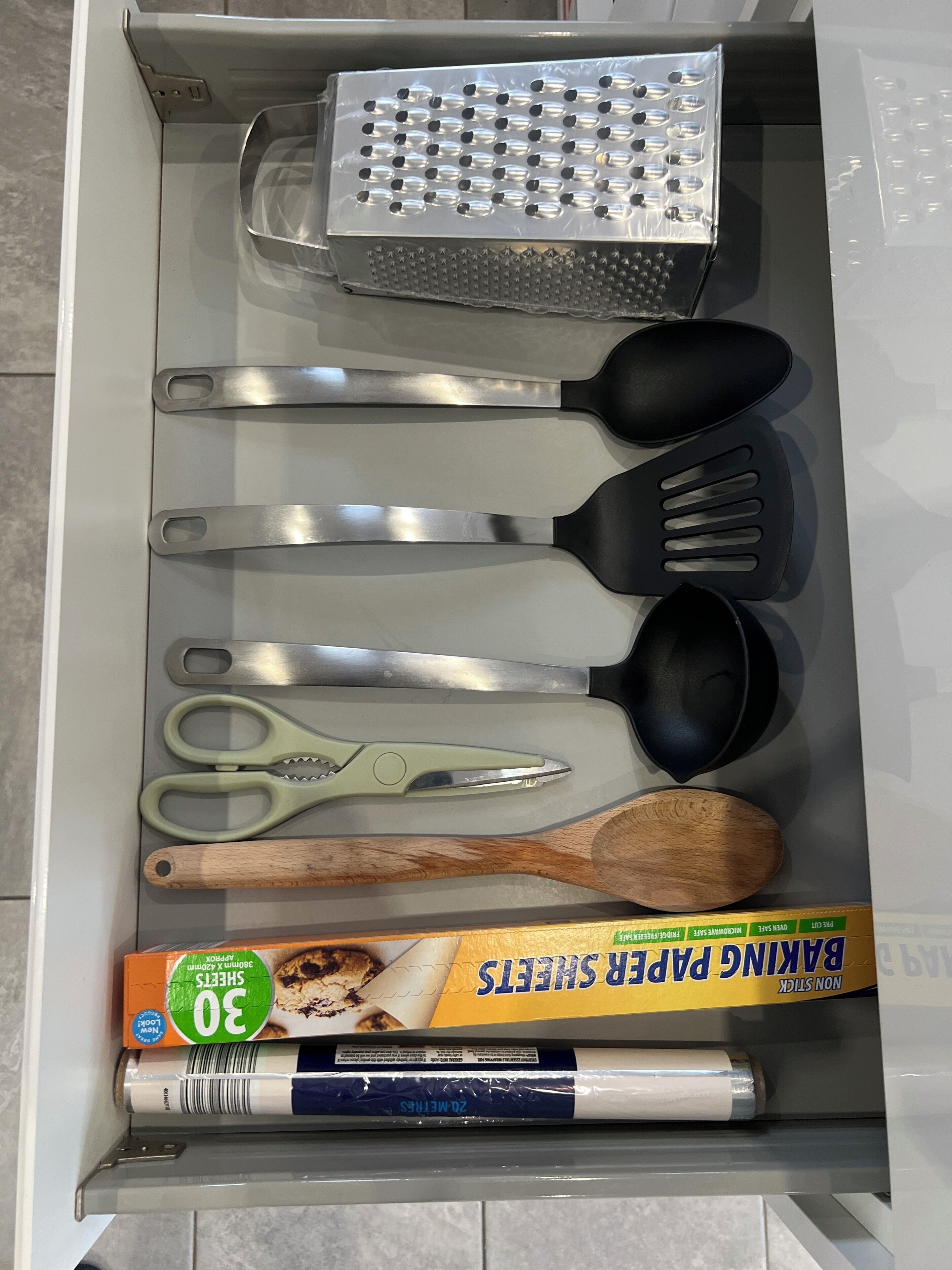 Un cajón con utensilios de cocina, incluyendo un rallador, espátulas, tijeras y una cuchara de madera.