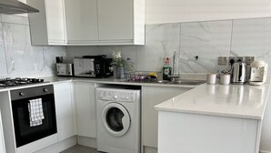 Una cocina moderna con armarios blancos, horno empotrado, lavadora y cafetera.