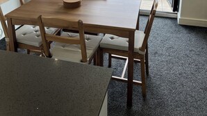 Una habitación con una mesa de comedor de madera, sillas acolchadas, una pequeña mesa redonda y vistas a un balcón con bicicletas y vegetación.