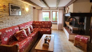A cozy living room with a red sofa, a wooden table, and a fireplace. - Authentic Vosgian farm, sauna, and beautiful view (LA BRESSE)