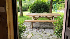 A wooden picnic table in a garden with stone paving, surrounded by greenery and trees. - Authentic Vosgian farm, sauna, and beautiful view (LA BRESSE)