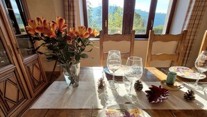 A dining table set with plates, cutlery, and wine glasses, with a vase of flowers and a view of the outdoors. - Authentic Vosgian farm, sauna, and beautiful view (LA BRESSE)