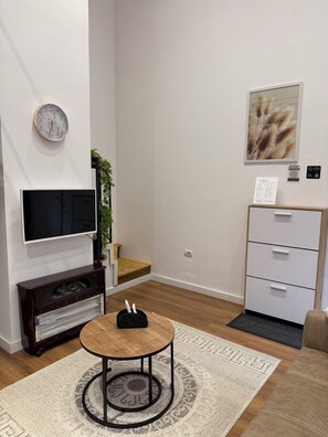 Un salon moderne doté d’un téléviseur à écran plat, d’une table ronde en bois, d’une cheminée, d’un meuble blanc et d’une horloge murale décorative.