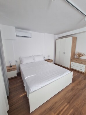 Ein modernes Schlafzimmer mit einem großen Bett, Holzboden, weißen Wänden und einem Kleiderschrank.
