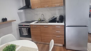A modern kitchen with wooden cabinets, a stainless steel refrigerator, and a built-in oven. - Stylish 1 Bedroom Duplex Apartment (Tiranë)